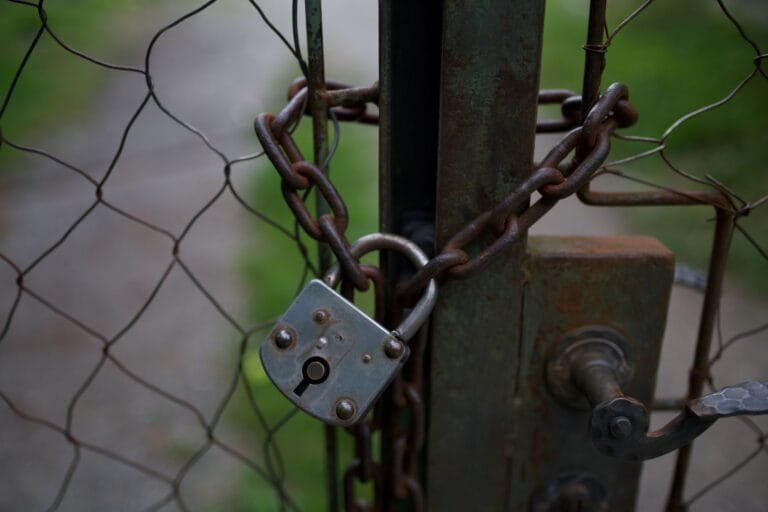 Encarregado de dados: por que sua empresa precisa de um e o que ele faz 7 A close-up of a rusty padlock and chain securing a metal fence gate, outdoors.