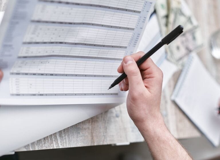 A close-up of a person holding a pen reviewing a financial document with cash visible, ideal for business themes.