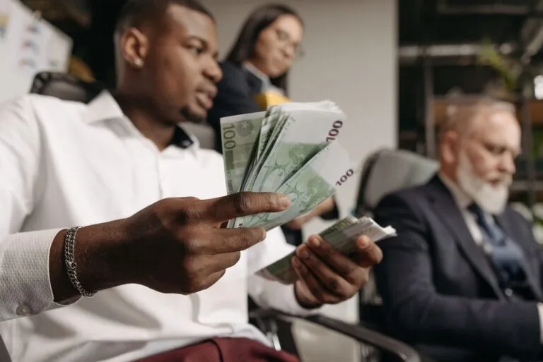 Equiparação salarial do bancário na mesma função por salário menor 7 Three professionals in business attire counting cash in a modern office setting.