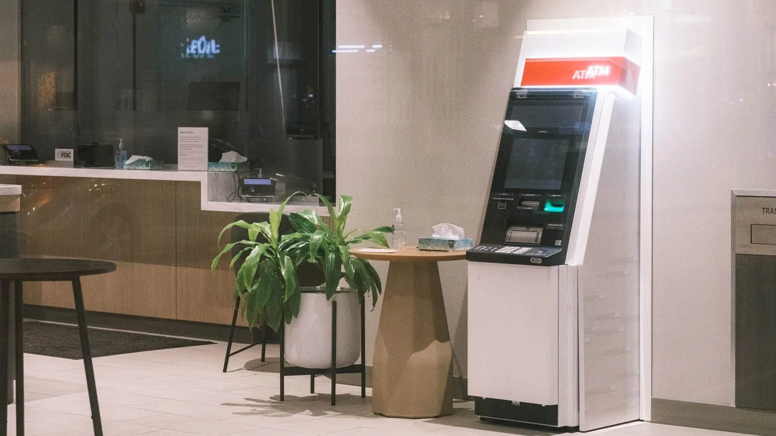 Estabilidade acidentária de doze meses do bancário adoecido 1 An ATM machine stands in a modern bank lobby, next to a plant and table.