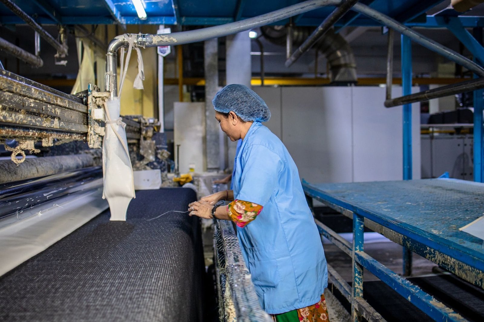 A female textile worker operates machinery in a factory, showcasing industrial production.