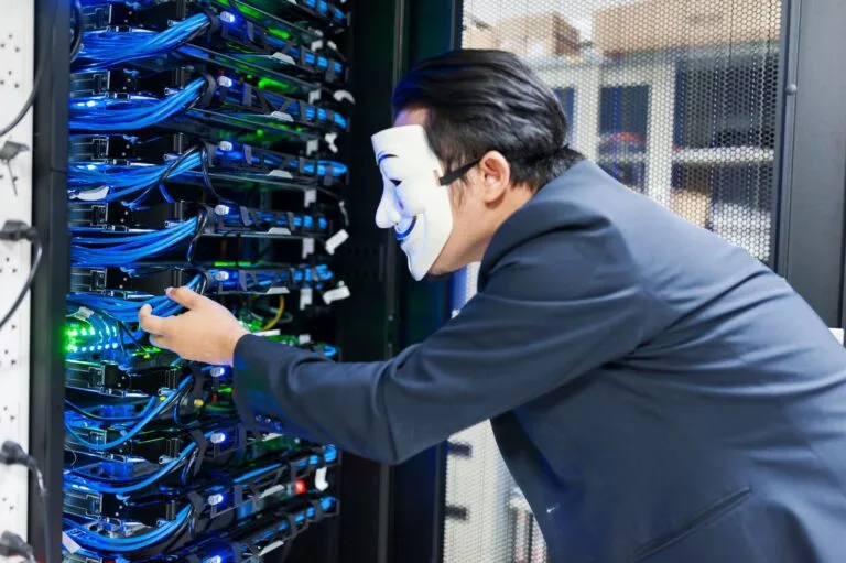 Estelionato: O Que Configura o Crime e Como se Proteger 2 Masked individual interacting with server racks, symbolizing cybersecurity threats.