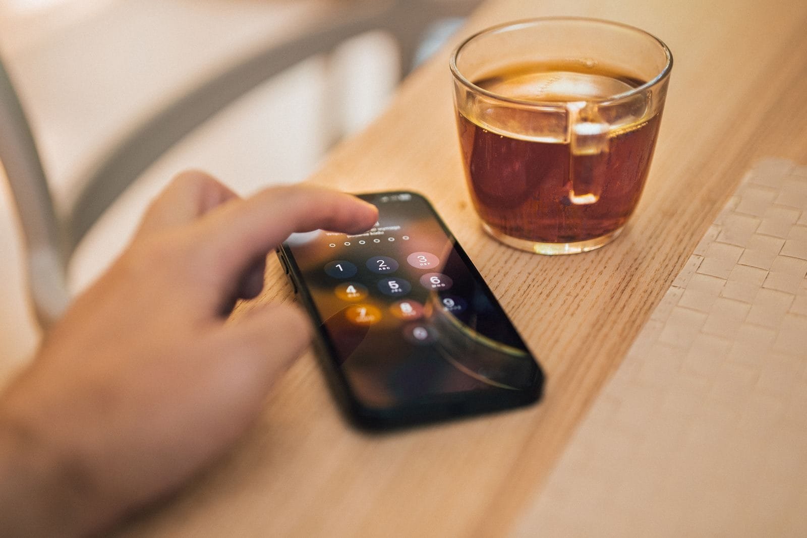 Estelionato digital: como funciona a responsabilidade dos bancos 1 Close-up of hand unlocking a smartphone next to a cup of tea on a wooden table, emphasizing technology and security.