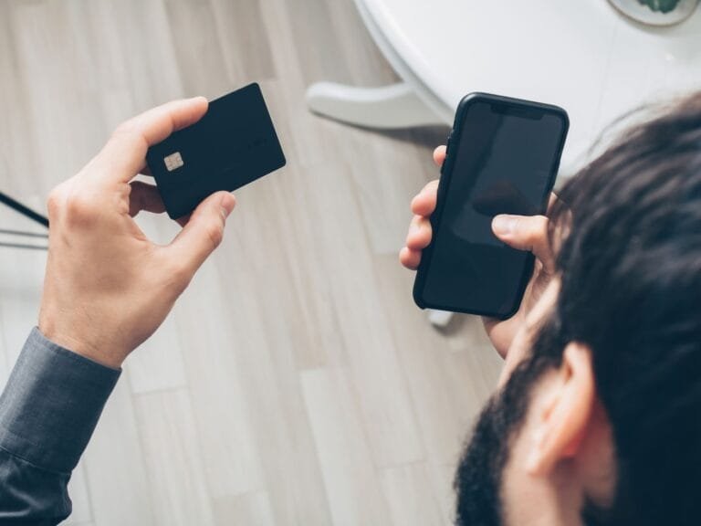 Estelionato digital: como reconhecer golpes do Pix e reagir aos primeiros sinais 6 Close-up of man holding a smartphone and credit card, making an online payment indoors.