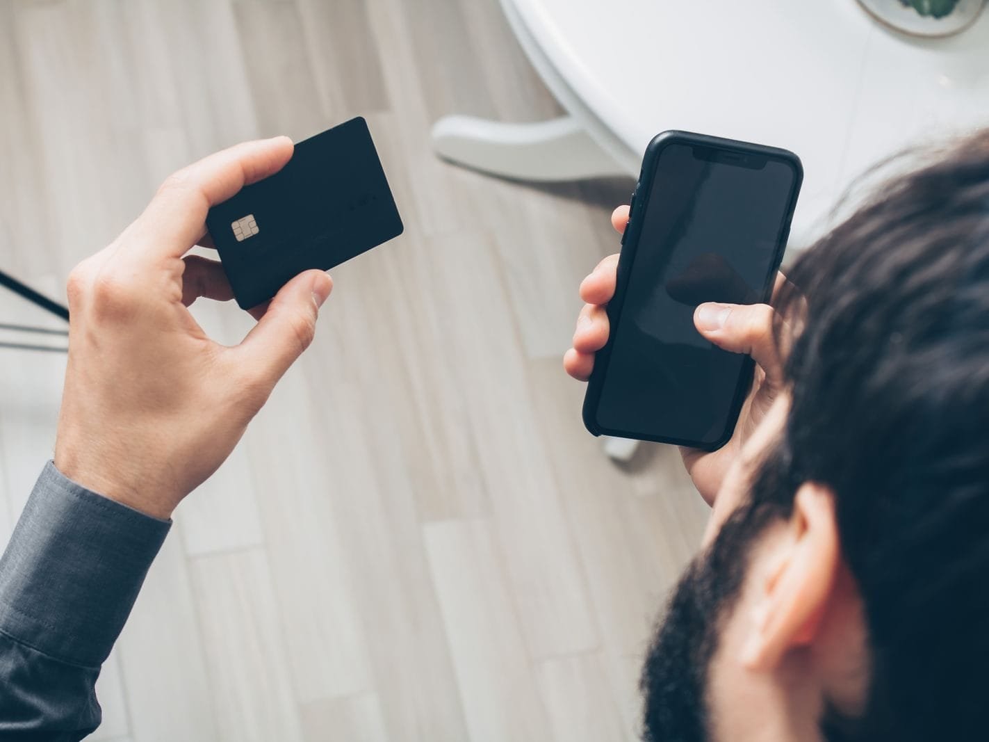 Estelionato digital: como reconhecer golpes do Pix e reagir aos primeiros sinais 1 Close-up of man holding a smartphone and credit card, making an online payment indoors.