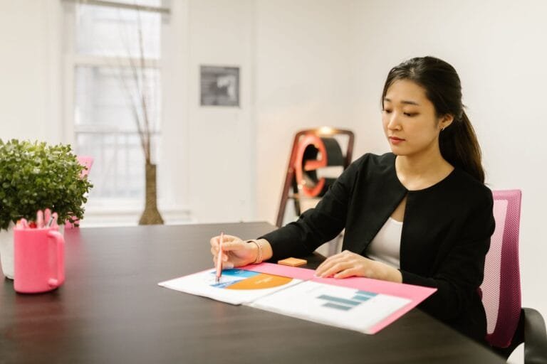 Woman in business attire analyzing documents at her office desk with reports and graphs.