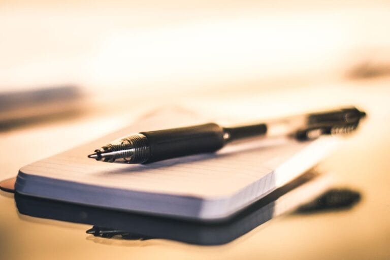 Resultados 12 Close-up of a black ballpoint pen resting on an open lined notebook with warm lighting.