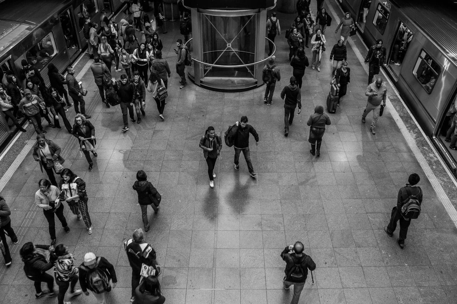 Black and white image of commuters in a bustling subway station, captured from above.