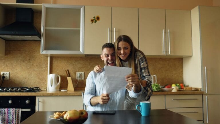 A happy couple celebrating good news at the kitchen table, adding joy to their home.