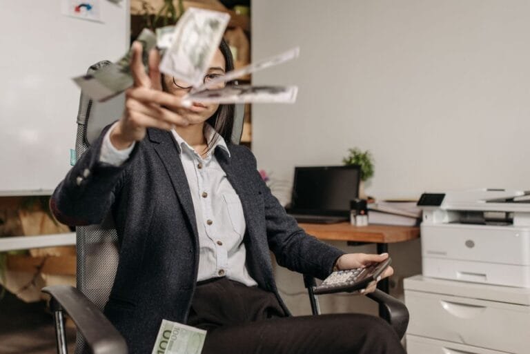 Gerente de banco: quando o cargo de confiança afasta a sexta hora 14 A businesswoman in a suit throws money while calculating finances in a modern office.