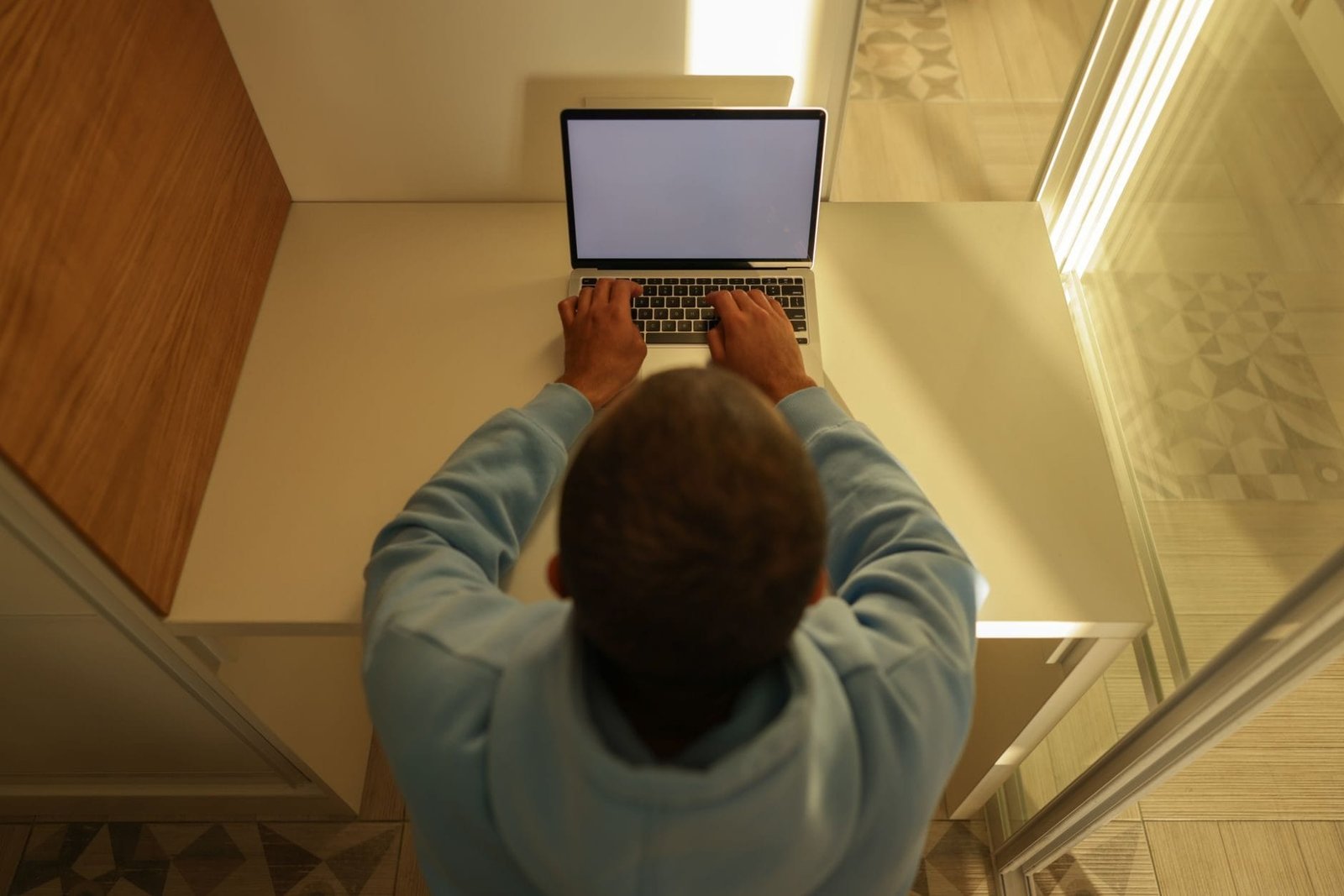 Overhead view of a man typing on a laptop with a blank screen, wearing a hoodie, sitting a
