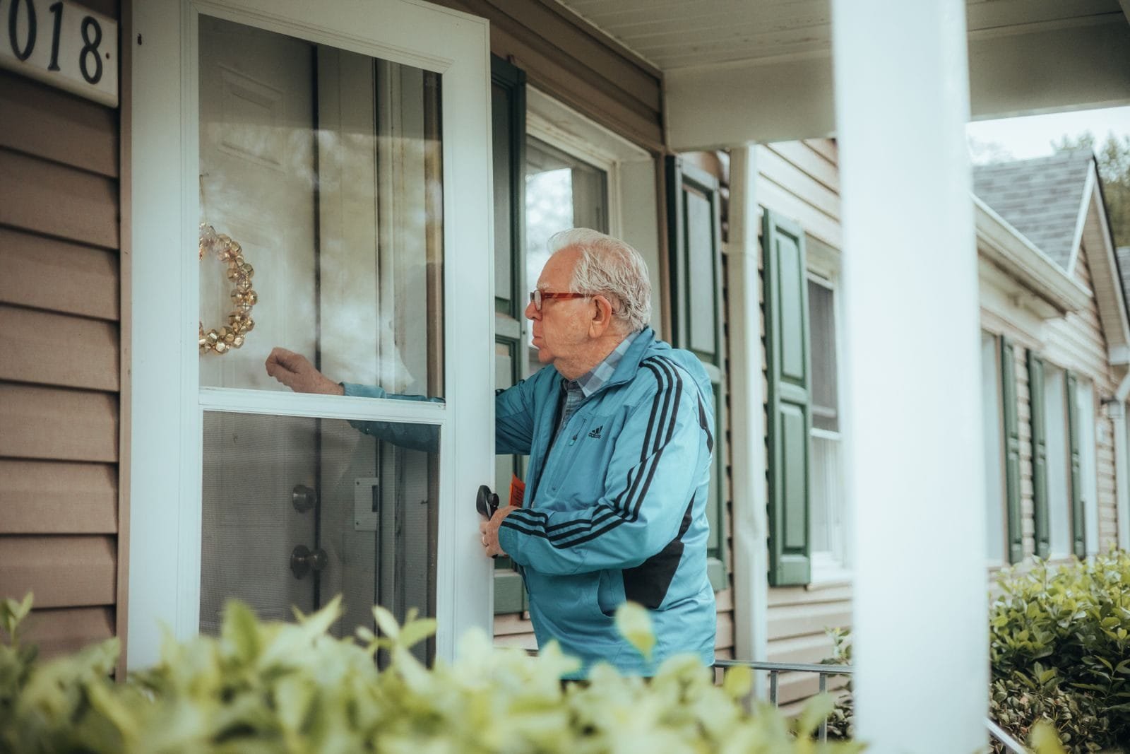 Elderly man in a blue jacket knocking on a suburban house door, showcasing community life.
