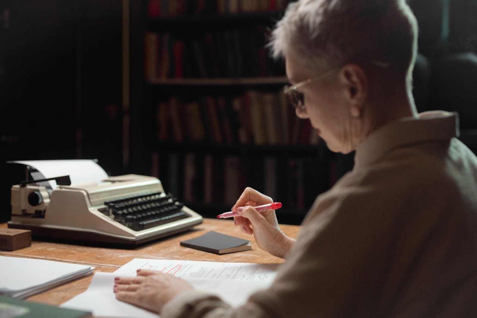 Governo Federal abre prazo para adesão ao acordo de ressarcimento de descontos indevidos no INSS 1 Elderly woman reviewing a manuscript with a typewriter at a wooden desk.