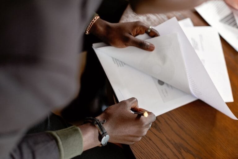 African American adult revising papers with a pencil at a desk, focus on hands and documen
