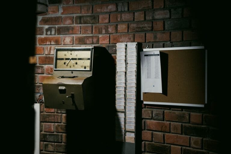 Horas extras e banco de horas: como saber se você está recebendo o que é devido 5 A retro time clock and stack of punch cards against a dark brick wall in an industrial setting.