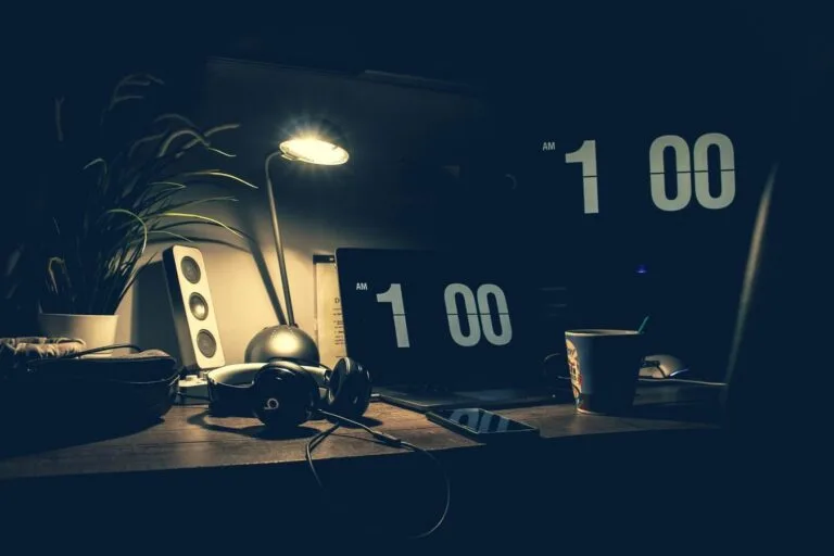Horas extras habituais do bancário elevam a média da aposentadoria 5 A dimly lit modern office desk with a laptop, headphones, and speakers at 1:00 AM.