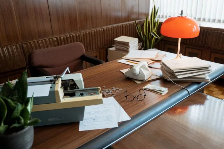 Improbidade administrativa: o que mudou no foco do dolo e quem responde 2 A retro office desk featuring a typewriter, vintage telephone, and stacks of documents.