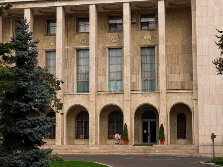 Exterior of a classical building with columns, arches, and greenery, showcasing elegant architecture.