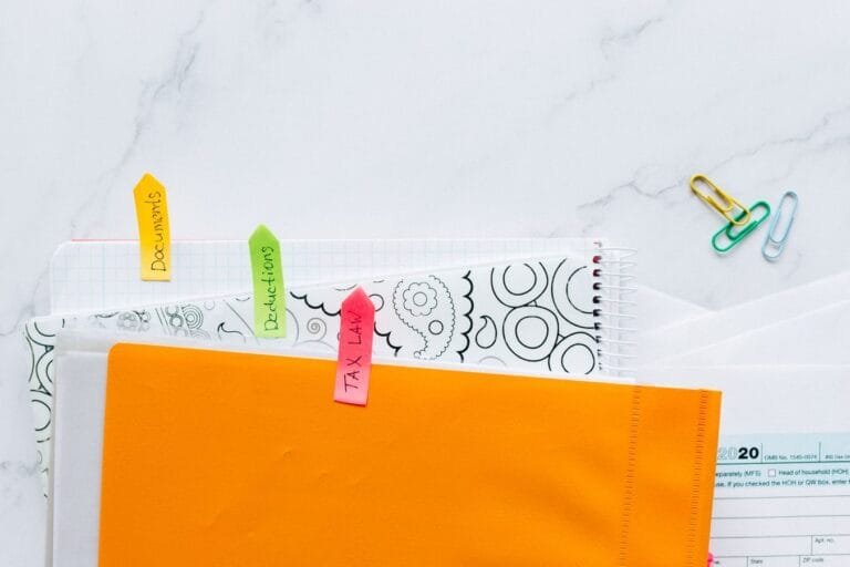 Como podemos ajudar? 1 Top view of tax documents organized with colorful sticky notes on a marble desk.