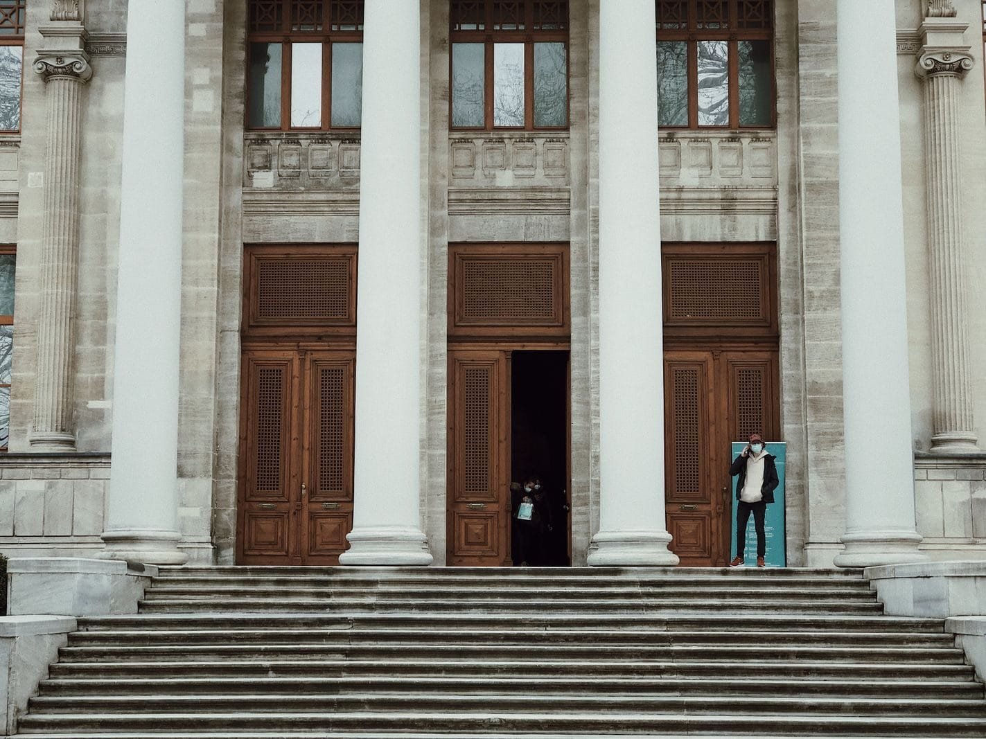 Exterior view of a neoclassical building with large columns and a staircase, featuring a person entering.