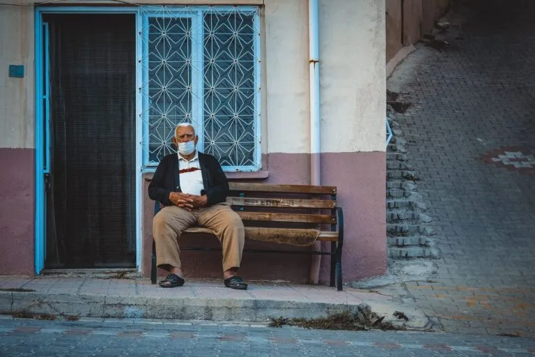 INSS Demora? Como Usar Mandado de Segurança para Resolver 2 Elderly man with face mask sitting on a bench in front of an urban building.
