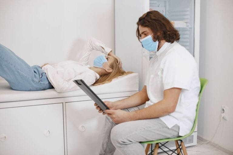 INSS faz mutirão nacional com mais de 37 mil perícias médicas em 132 agências nos dias 28 e 29 de março de 2026 12 Doctor consulting patient wearing face masks in a medical examination room, discussing healthcare plan.