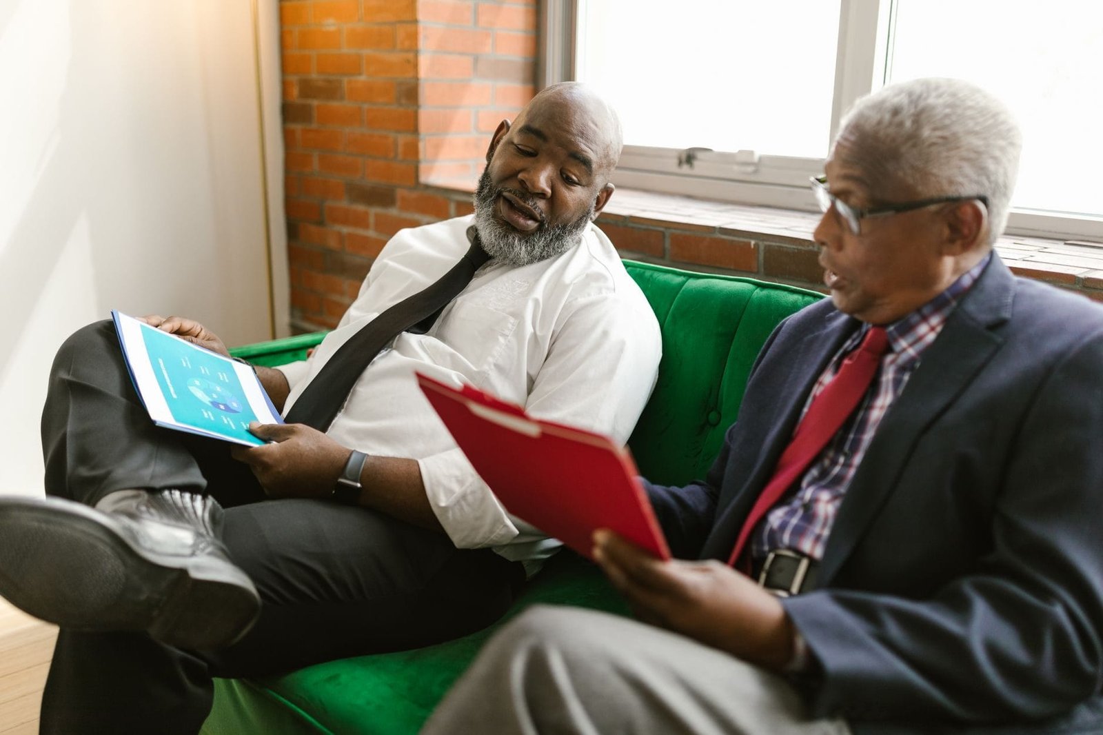 Two senior men in business attire discussing reports on a sofa.