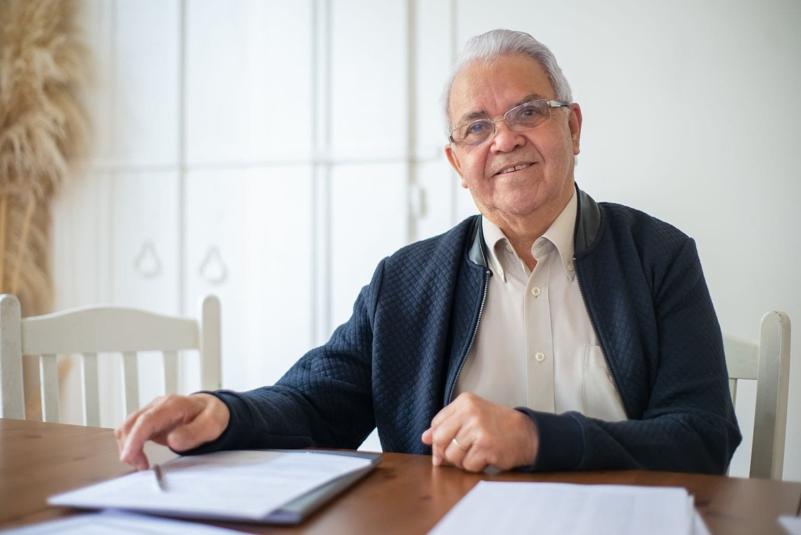 INSS notifica 4 milhões de beneficiários para prova de vida manual após falha do cruzamento automático (outubro/2025) 1 Senior man with glasses reviewing paperwork at a table, showcasing concentration.