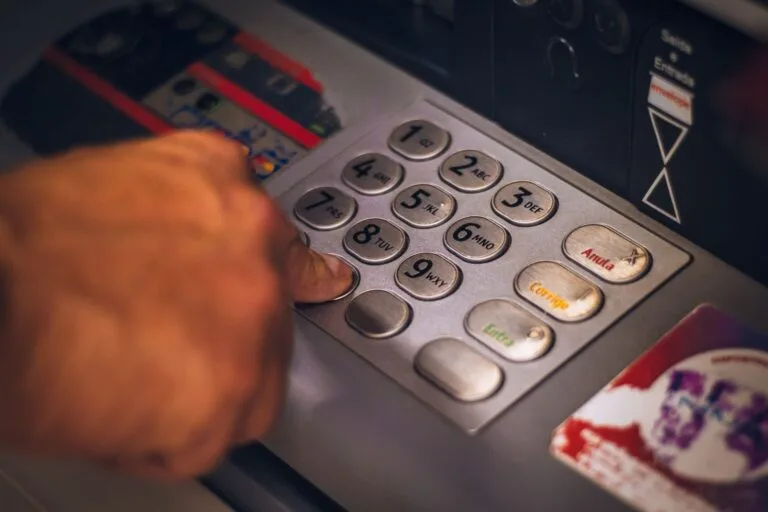 INSS Inicia Pagamento de Benefícios de Fevereiro em 2026 7 A hand pressing a button on an ATM keypad in Brasil, emphasizing digital banking.
