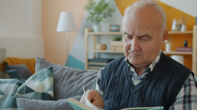 Elderly man reading a book on a couch.