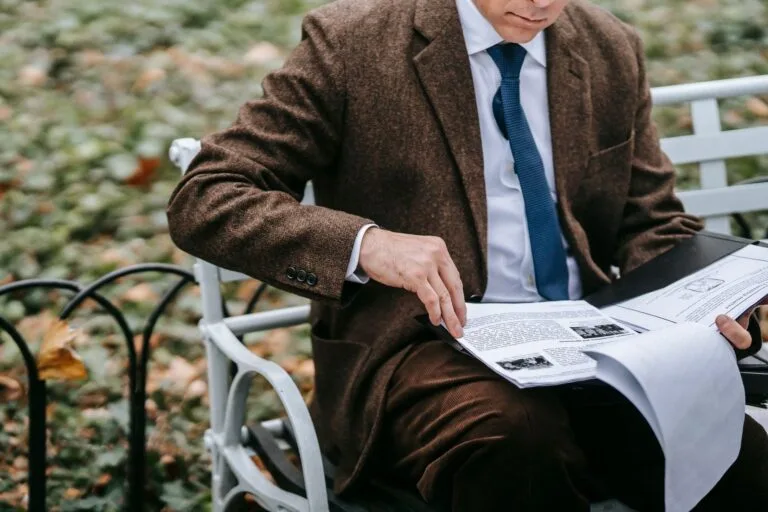 A businessman in formal attire reviewing documents on an outdoor park bench.