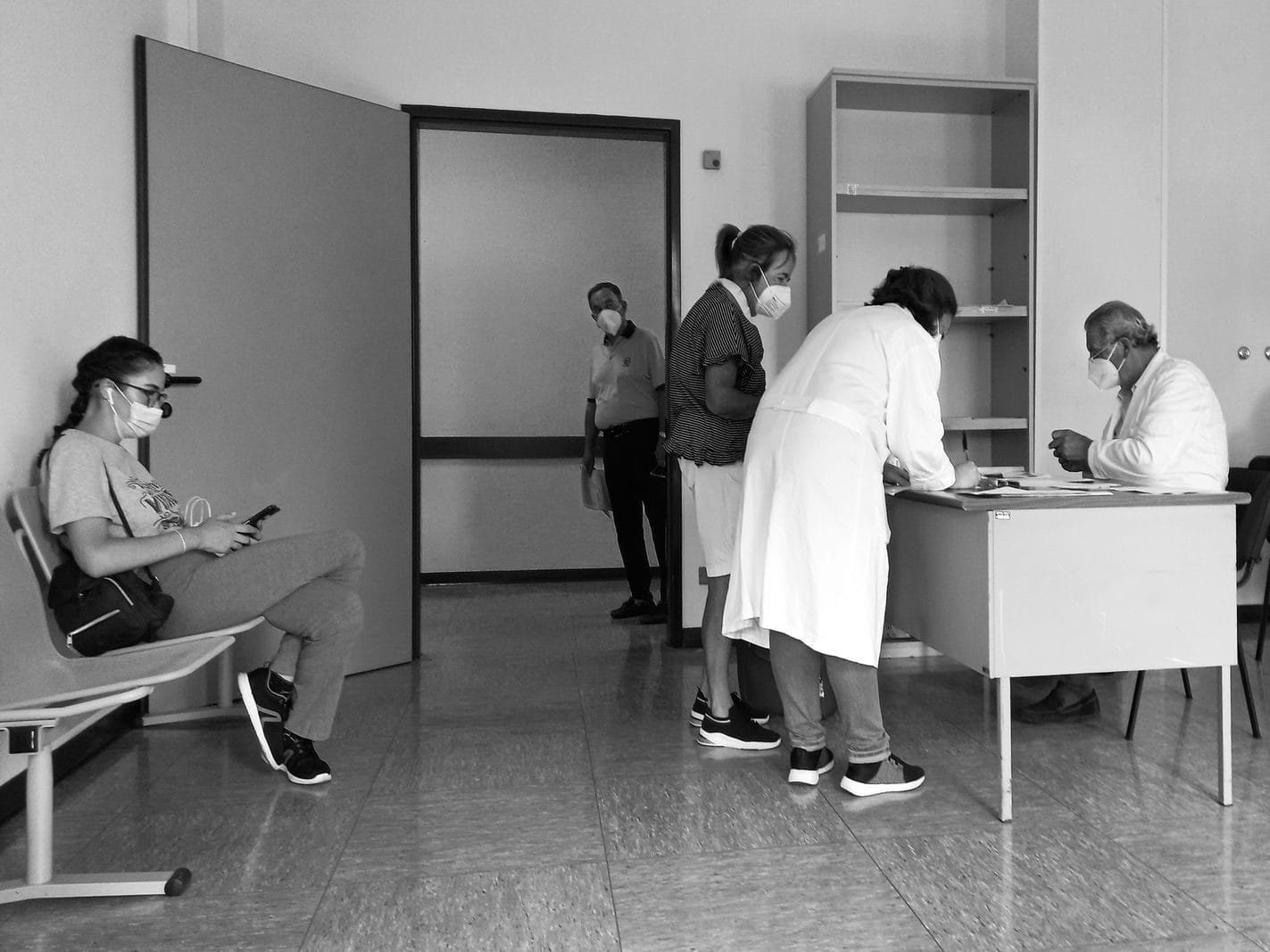 Black and white photo of a hospital waiting room with people wearing masks.