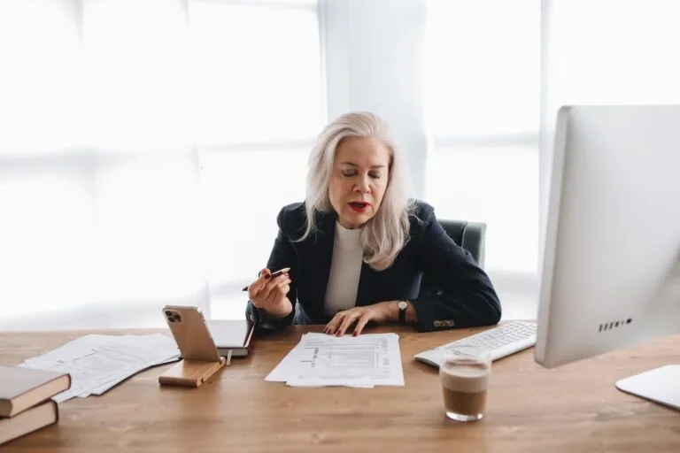 Isenção de IR Aposentado 2026: Lista de Doenças Graves 2 Senior woman in office reviewing financial documents with focused expression.