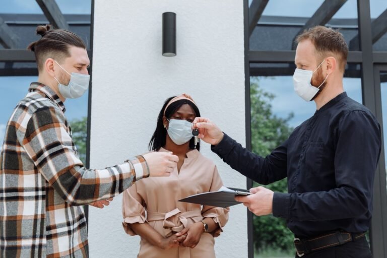 Real estate agent handover keys to a diverse couple wearing face masks, outdoors.