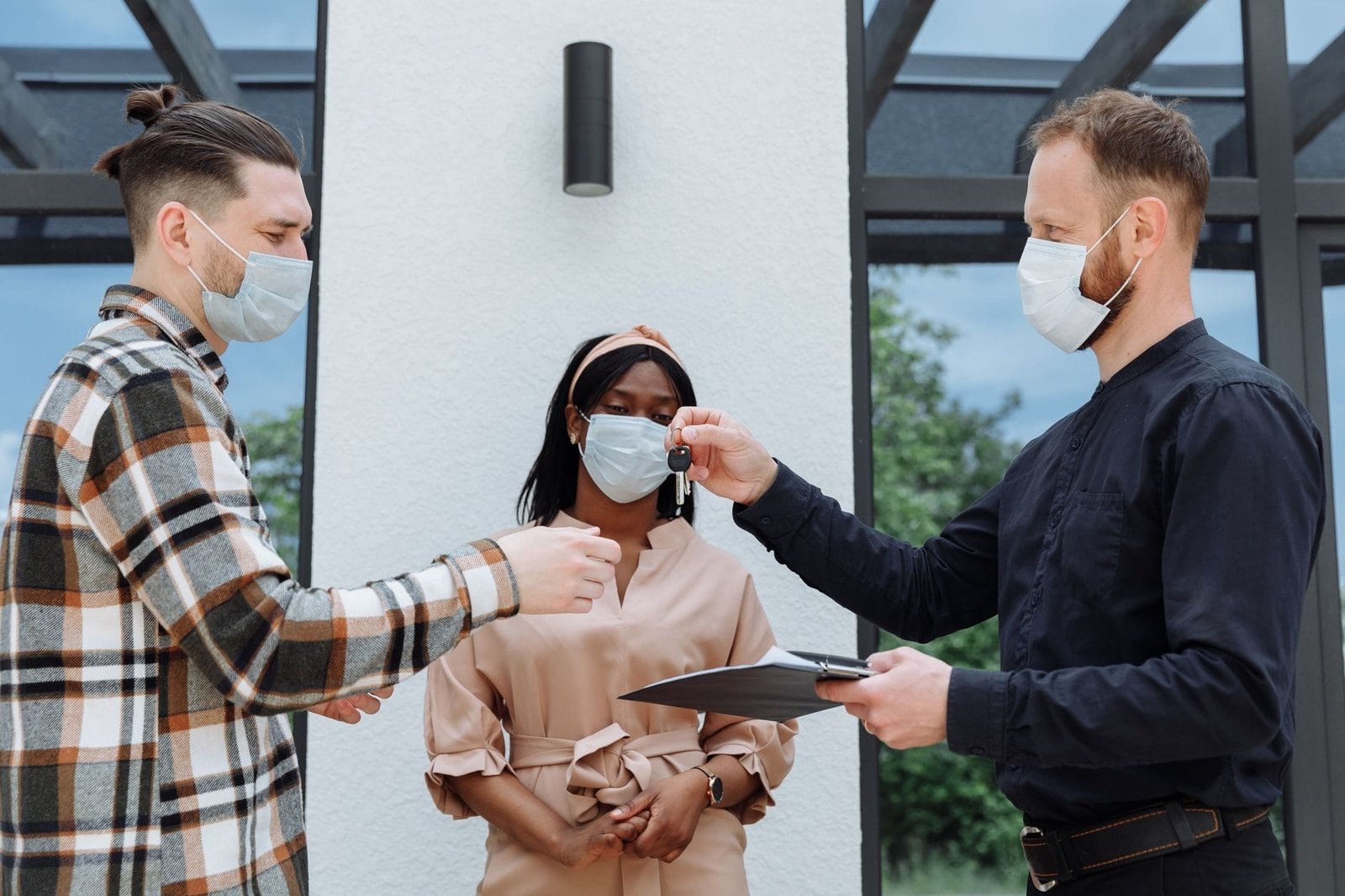 Legitima defesa da propriedade: ate onde se pode ir para proteger o imovel 1 Real estate agent handover keys to a diverse couple wearing face masks, outdoors.