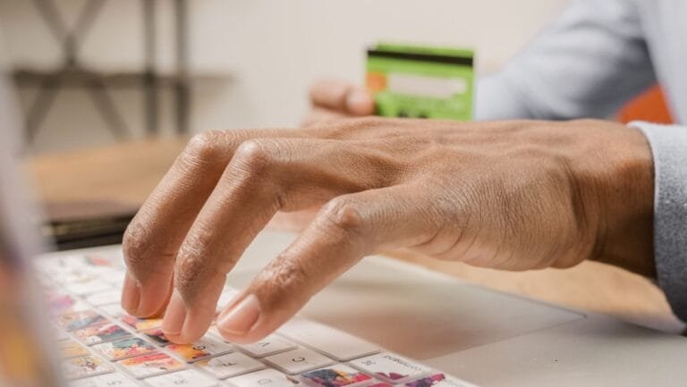 Person typing on a colorful laptop keyboard while holding a credit card, ideal for online shopping themes.