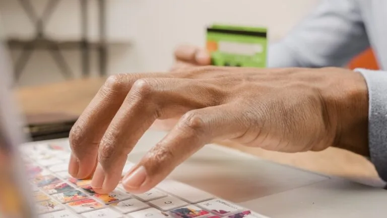 Person typing on a colorful laptop keyboard while holding a credit card, ideal for online shopping themes.