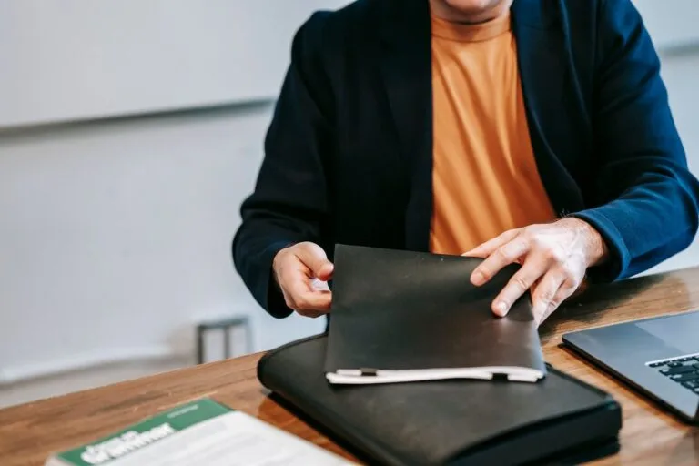 Licença para Tratar de Interesses Particulares do Servidor 4 A business professional in a blazer organizing documents at a wooden desk inside an office.
