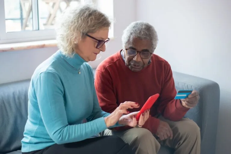 Lula sanciona Lei 15.327/2026 que proíbe descontos associativos no INSS e exige biometria ou assinatura eletrônica para liberar consignado 5 Elderly couple using a smartphone for online shopping, holding a credit card.