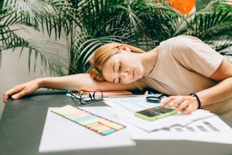 Malha fina do Imposto de Renda: por que cai e como regularizar a situação 3 A tired woman calculating her taxes at a desk covered with papers and a smartphone.