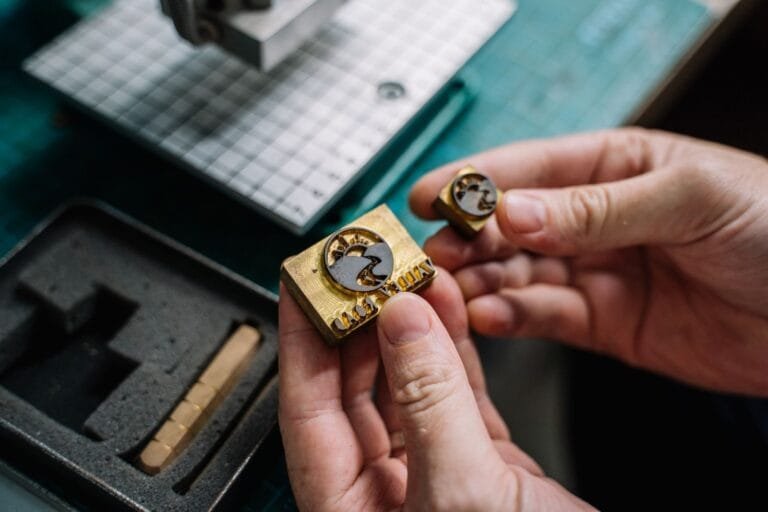Marca registrada: por que proteger o nome do seu negócio antes que outro registre 3 Close-up view of hands holding handcrafted brass stamps on a workbench.