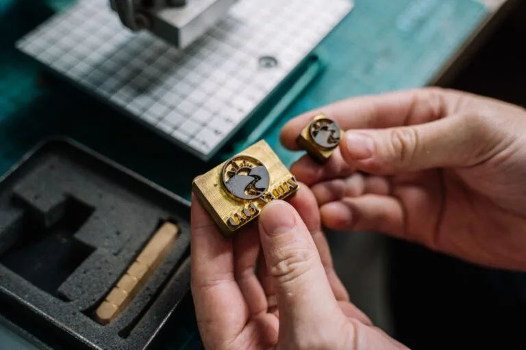Close-up view of hands holding handcrafted brass stamps on a workbench.