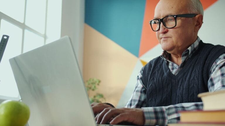 Medida Provisória 1.306/2025 abre crédito extraordinário de R$ 3,3 bilhões para ressarcir vítimas de fraudes no INSS 4 Elderly man focused on his laptop in a stylish, colorful office environment.