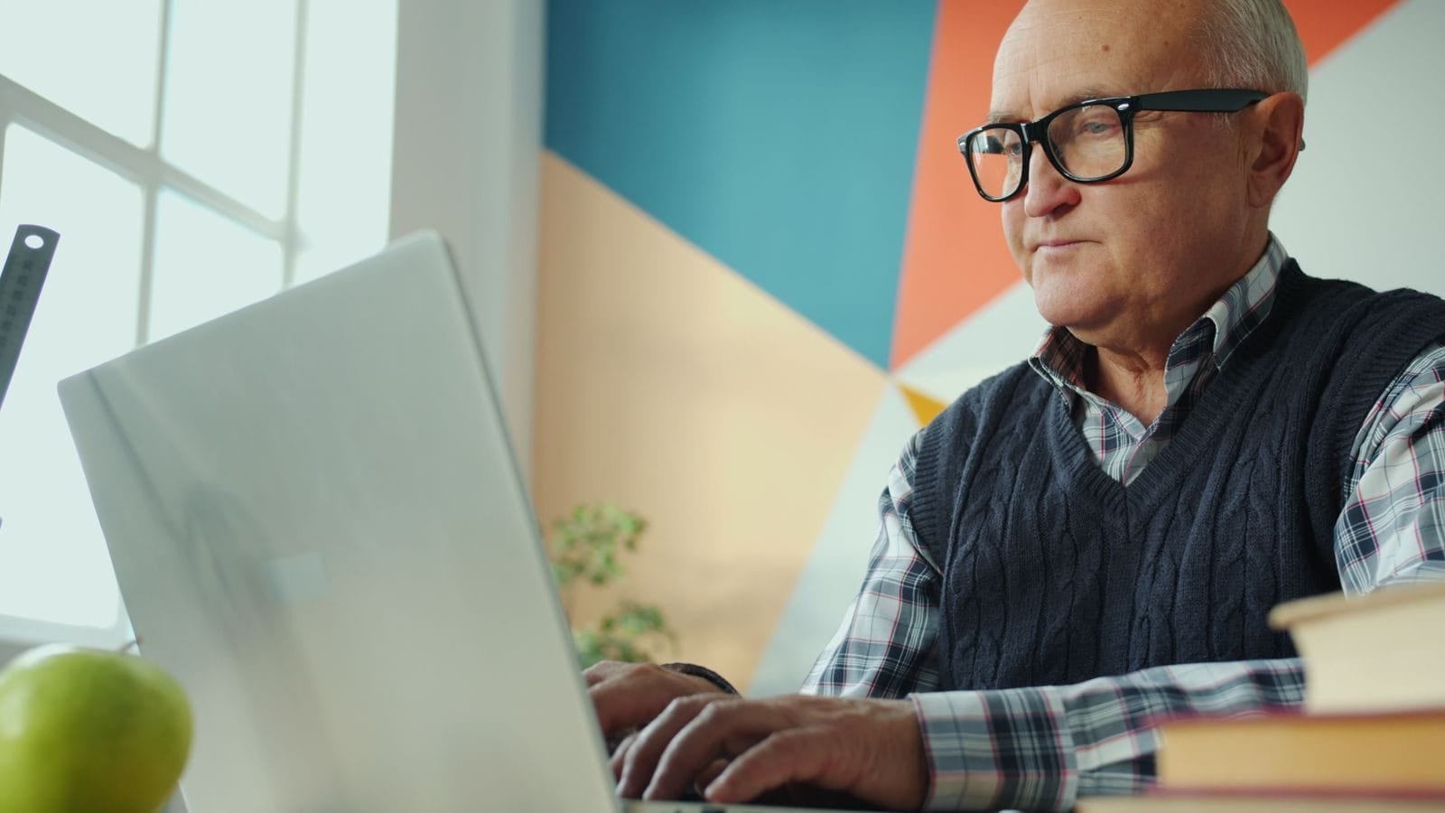 Medida Provisória 1.306/2025 abre crédito extraordinário de R$ 3,3 bilhões para ressarcir vítimas de fraudes no INSS 1 Elderly man focused on his laptop in a stylish, colorful office environment.