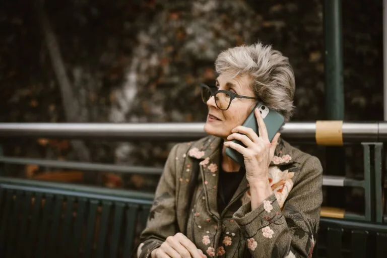Meu INSS: Como Usar o App, Pedir Benefícios e Resolver Tudo 7 Elderly woman with glasses talking on a smartphone while seated outdoors.