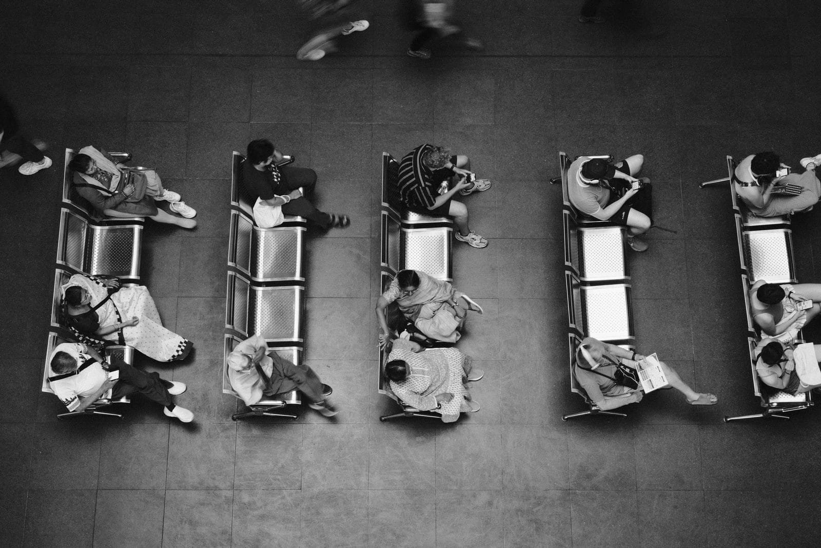 Black and white high angle photo of people sitting and waiting at a station.