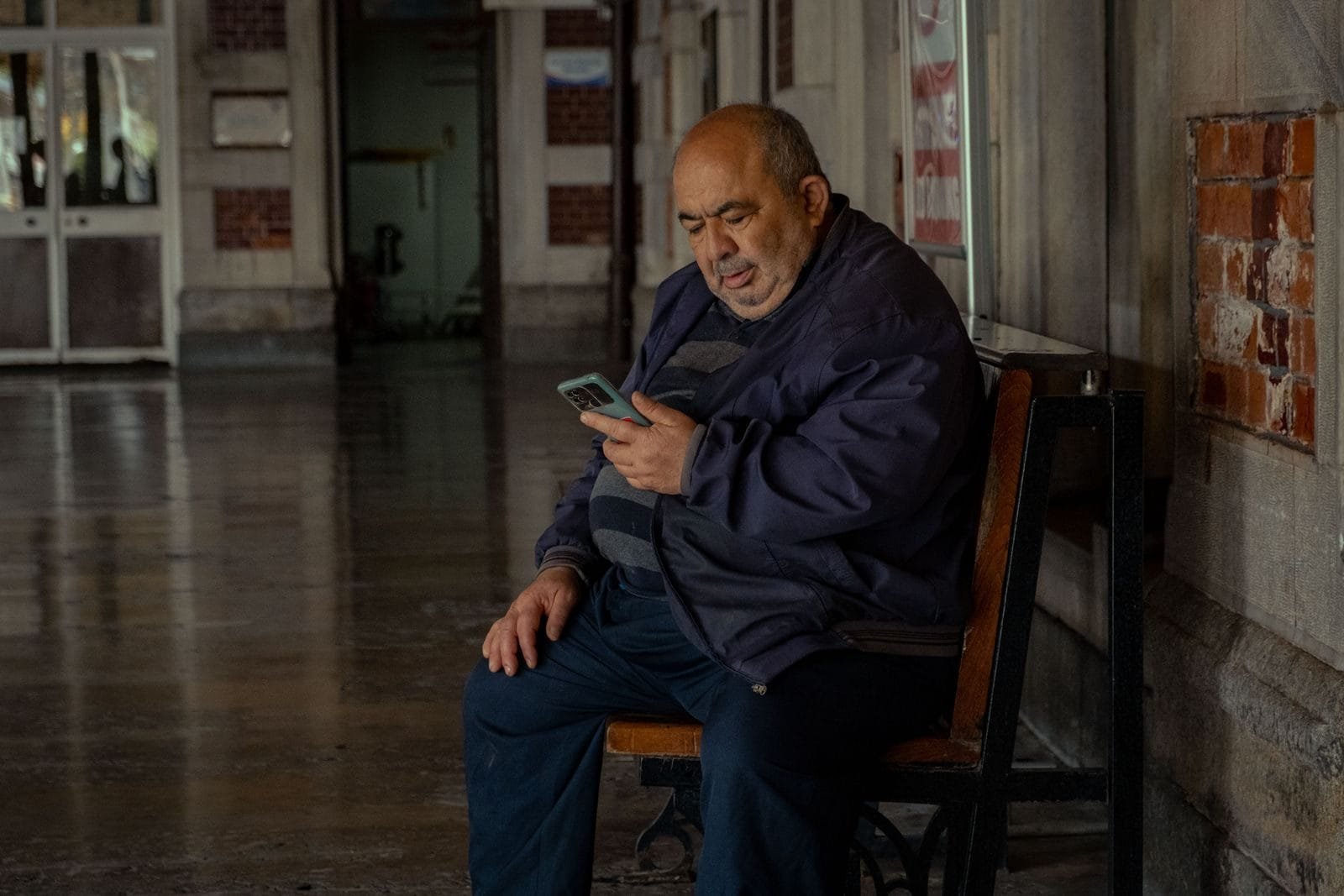 Adult man sitting on bench indoors, using smartphone for communication.