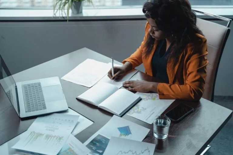 O dever de motivar: por que toda decisão administrativa precisa explicar suas razões 2 Businesswoman in office writing notes with documents and laptop, focused on analysis and productivity.