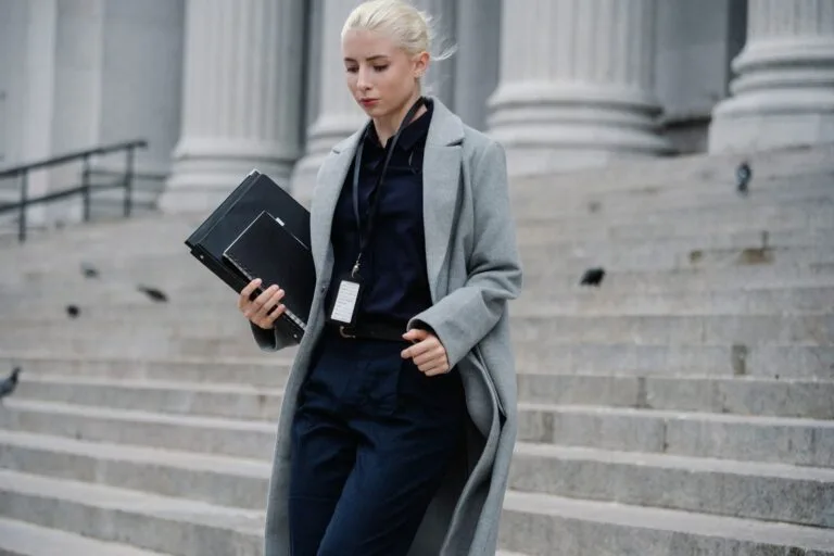 O que é improbidade administrativa e quem pode ser responsabilizado 4 Young stylish female lawyer in formal clothes with name tag holding folders while going downstairs near stone building w