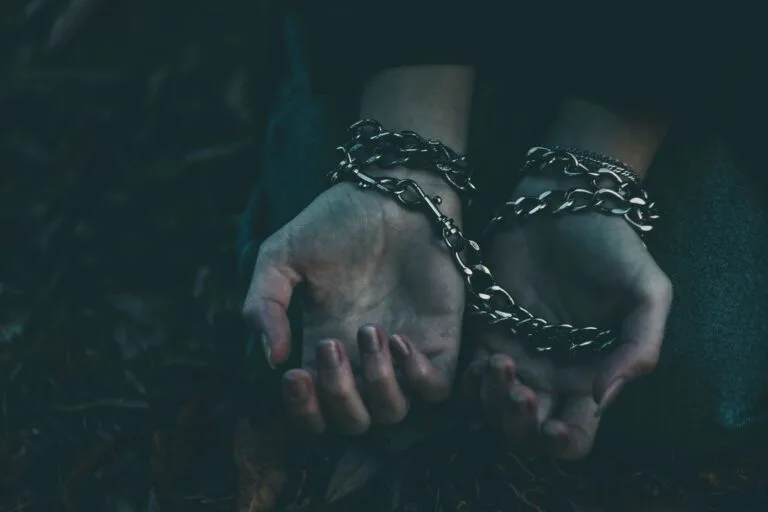 A dramatic close-up image of hands bound by silver chains, symbolizing captivity or struggle.